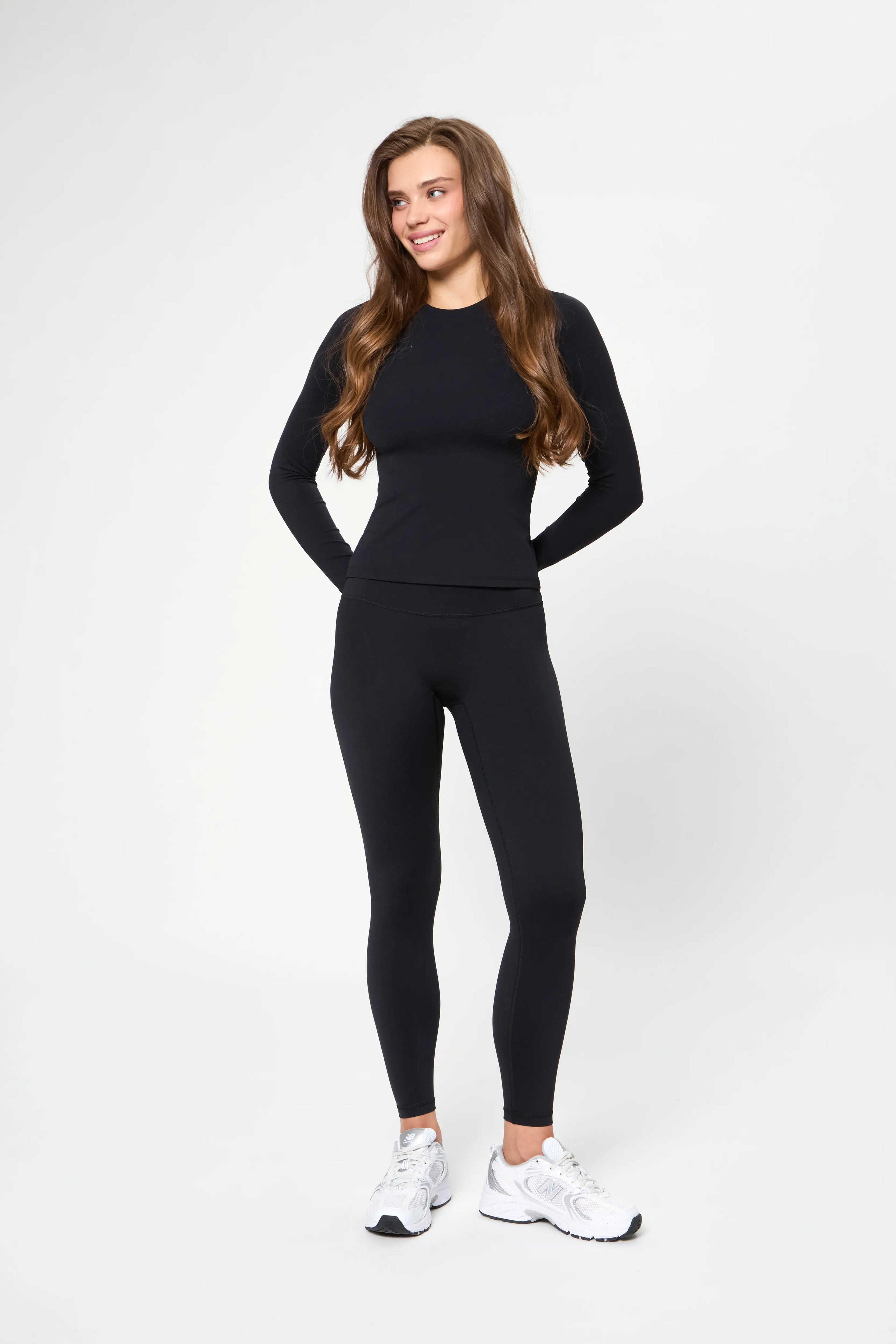 Woman wearing black leggings and long sleeve top smiling against white background Базові легінси чорного кольору