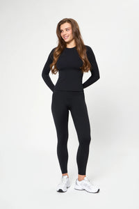 Woman wearing black leggings and long sleeve top smiling against white background Базові легінси чорного кольору