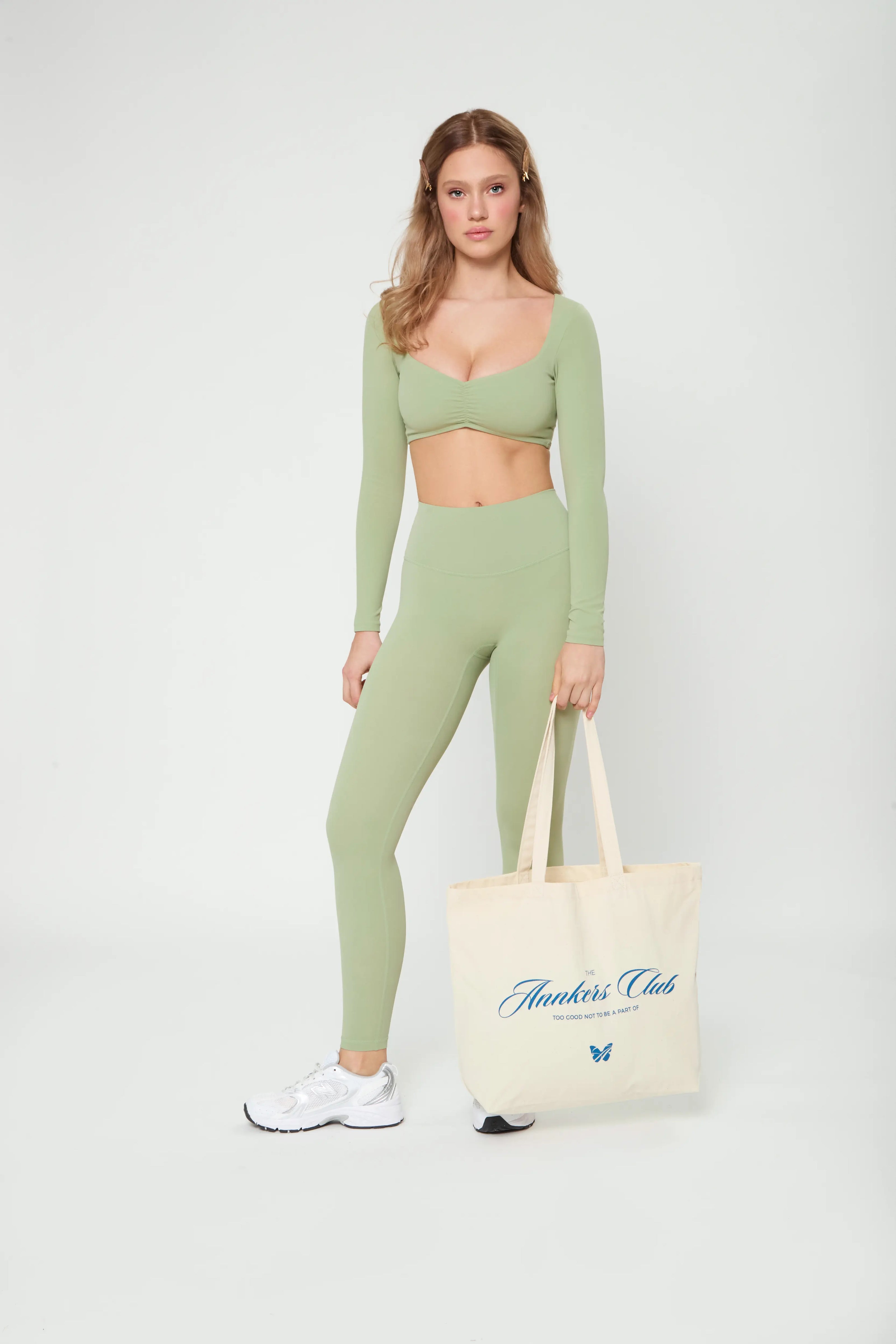 Model wearing Базові легінси оливкового кольору leggings with high waist, holding a tote bag and white sneakers.